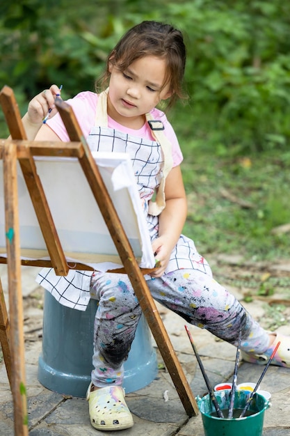 Carino piccolo artista pittura immagine pittura su tela nella foresta della natura bambina felice in giardino