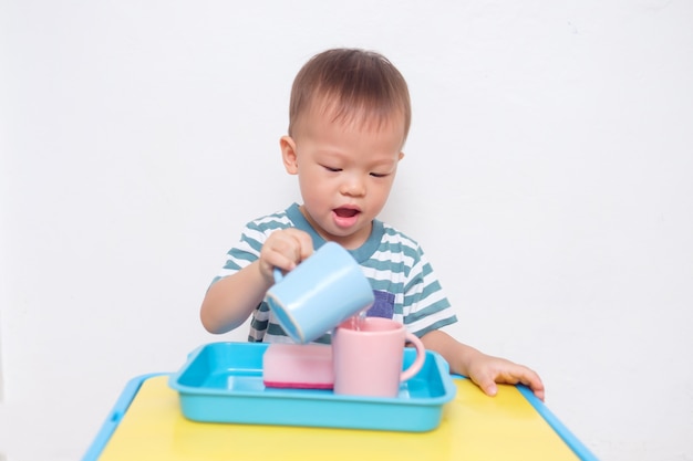 Carino piccolo asiatico 2 anni bambino ragazzo bambino divertirsi versando acqua nella tazza, attività di vita pratica in età prescolare montessori versando bagnato, abilità motorie, concetto di sviluppo del bambino senso dei bambini