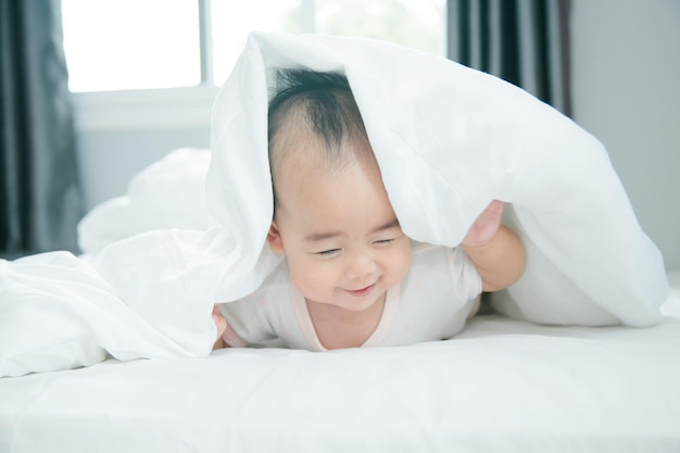 Cute little asian baby on bed with soft blanket indoors