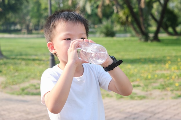 Carino bambino asiatico che beve acqua pura da una bottiglia d'acqua riutilizzabile sulla natura nel parco