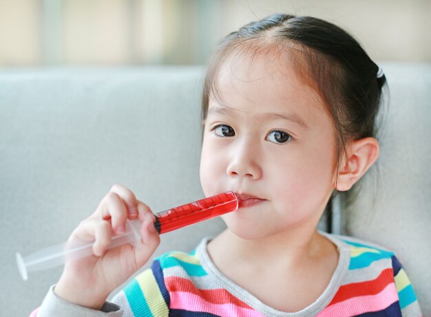 かわいいアジアの子供の女の子彼女の口の注射器で薬を摂食。