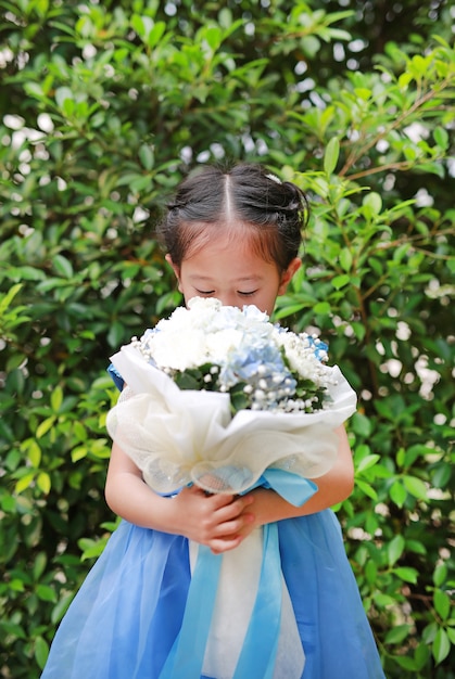 Piccola ragazza asiatica sveglia del bambino che sente l'odore mazzo dei fiori nel giardino.