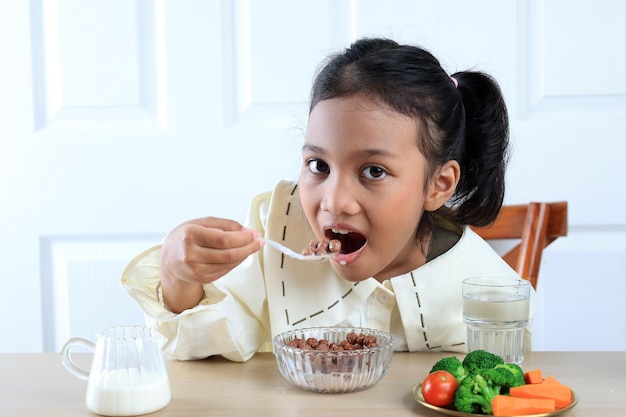 Photo cute little asian girl eating chocolate cereal