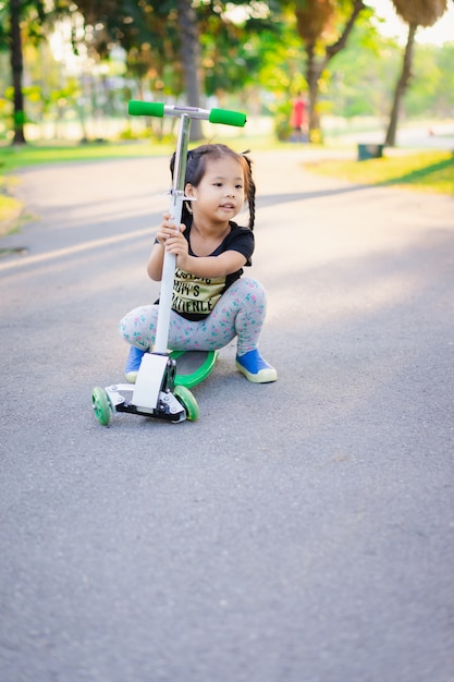 Cute little asian girl learning to ride a scooter in a park