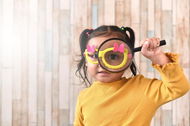 Photo cute little asian girl looking through a magnifying glass