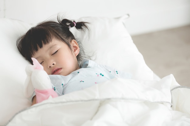 ベッドで人形で眠っているかわいいアジア人少女