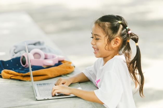 야외 공원에서 노트북 컴퓨터를 사용하는 귀여운 작은 아시아 소녀