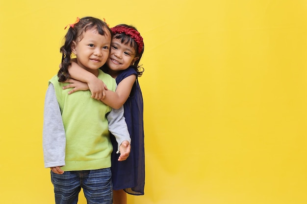 Милые азиатские девушки улыбаются и обнимают свою подругу на желтом фоне с копировальным пространством