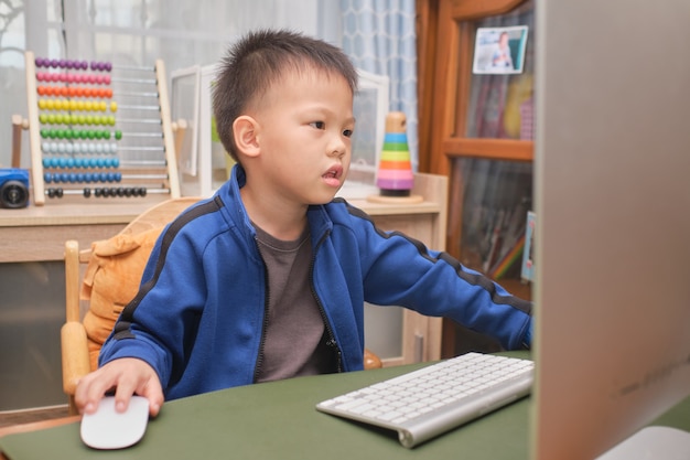 Cute little Asian kid with personal computer making video call at home, Kindergarten boy concentrate on studying online, attending school via e-learning