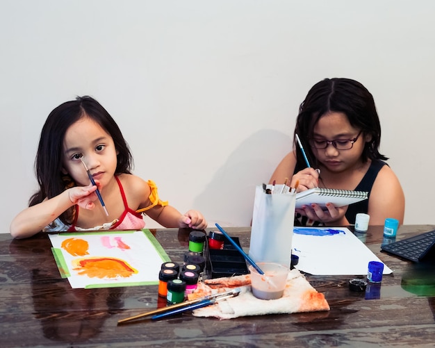 Cute little asian siblings painting a picture in home studio