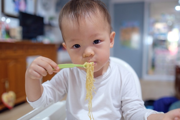 かわいい小さなアジア幼児赤ちゃん男の子子供はフォークで麺を食べる