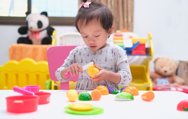 Cute little asian toddler baby girl child having fun playing alone with cooking toys