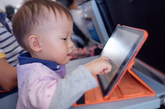 Cute little Asian toddler boy child using tablet pc watching cartoons during flight on airplane