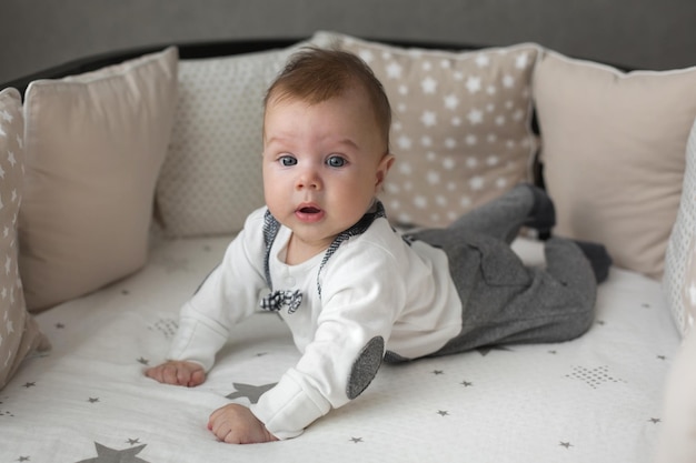 A cute little baby boy infant is lying on the bed in kids room