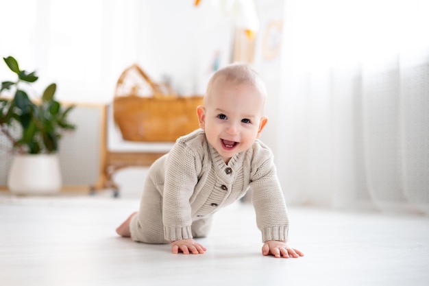 Foto simpatico neonato in un abito lavorato a maglia di lana pastello che impara a gattonare sul pavimento in un soggiorno luminoso bambino sorridente che gioca lo sviluppo iniziale dei bambini