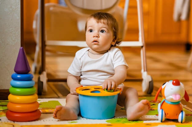 Cute little baby boy playing with colorful educational toys on the play mat in the home interior