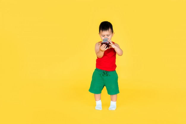 Piccolo neonato sveglio in maglietta rossa e breve verde con la tazza di succo su giallo