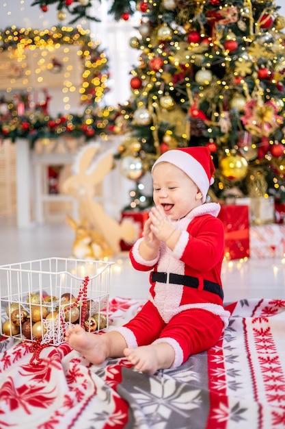 サンタの衣装を着たかわいい男の子がクリスマス ツリーのおもちゃで座っています。