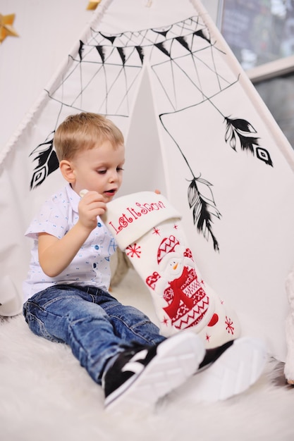 Cute little baby boy takes out a present from a Christmas sock against the background of a tent or an Indian wigwam