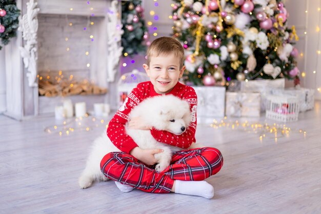 Милый маленький мальчик с белым щенком самоеда возле елки, концепция праздника, новый год