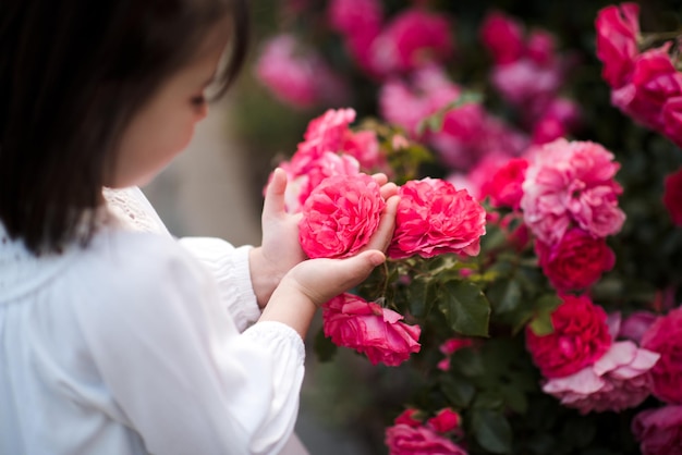 Foto piccola bambina carina di 3-4 anni che tiene delle rose rosa in giardino close-up stagione estiva infanzia