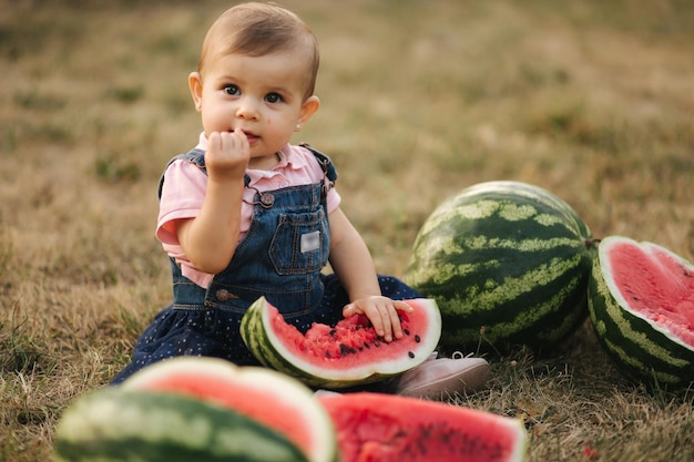 Photo cute little baby girl laughing with watermelons girl dressed in denim dress summer portrait of child