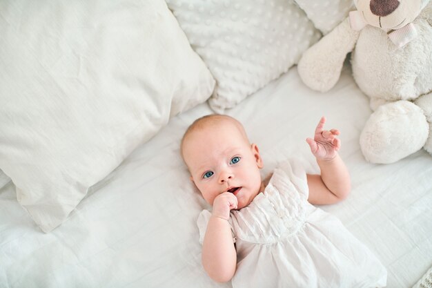 Cute little baby girl lying on bed, finger in mouth.