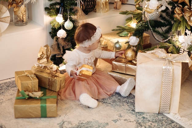 Cute little baby girl near the Christmas tree with gifts