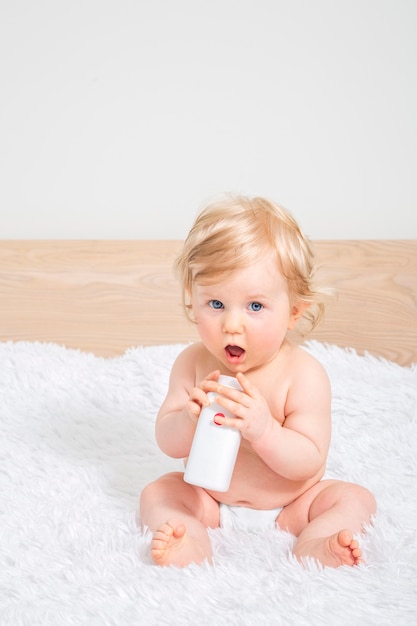 Cute little baby girl with bottle of baby oil in parent bedroom.