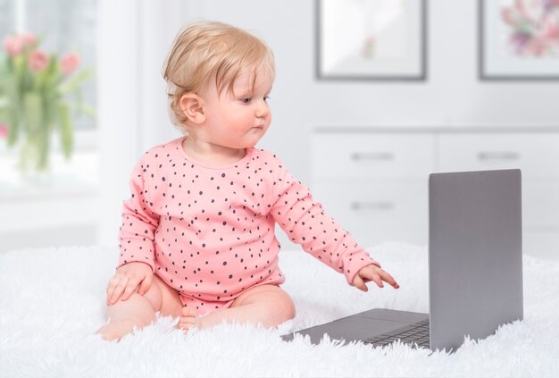 Cute little baby girl with laptop in parent bedroom