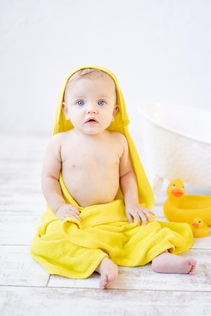 Cute little baby girl under a yellow towel in the bathroom after bathing or washing baby hygiene concept