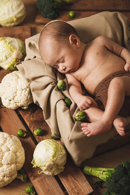 Cute little baby is lying in the box with a lot of different cabbages around