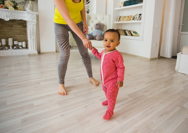 Cute little baby learning to walk, mom is holding his hands.