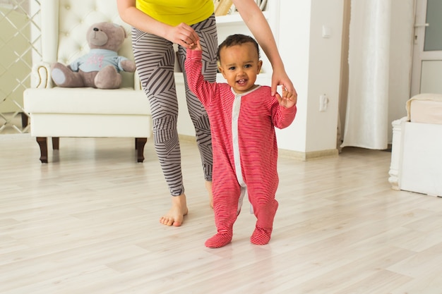 Cute little baby learning to walk, mom is holding his hands.