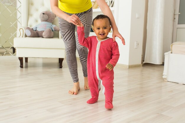 Cute little baby learning to walk, mom is holding his hands.