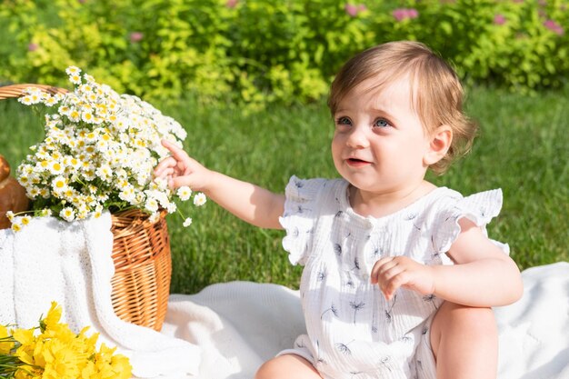 Photo cute little baby on picnic with flowers and organic fruits in the summer park sunny day