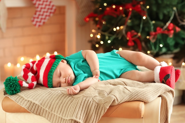 Cute little baby sleeping against blurred Christmas lights surface