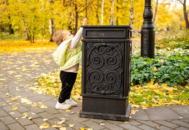 Il piccolo bambino carino getta la spazzatura nel bidone della spazzatura nel parco autunnale instillando le norme culturali dalla nascita