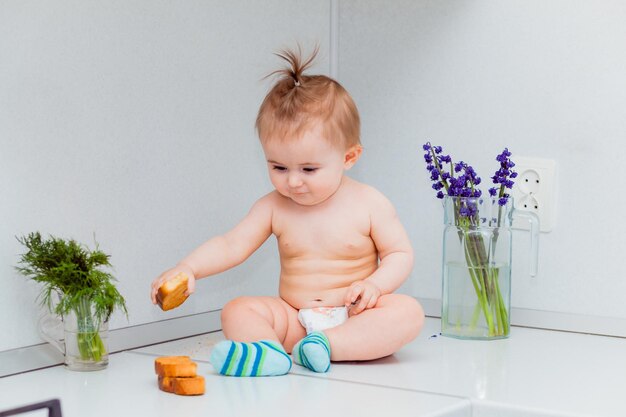 Cute little baby with cookies sitting on the table in the kitchen