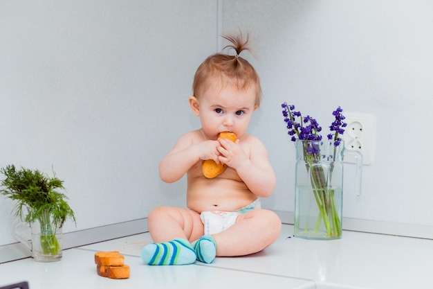 Cute little baby with cookies sitting on the table in the kitchen