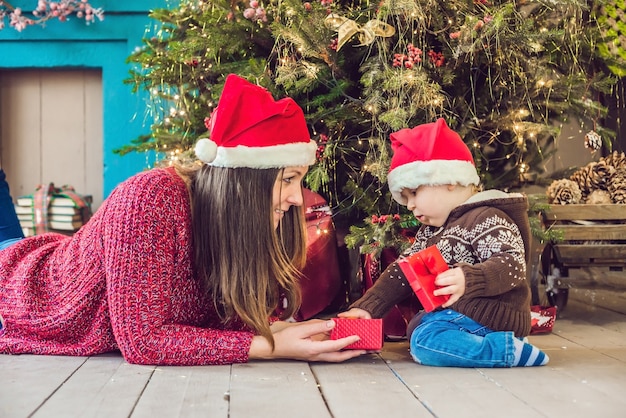 Cute little baby with his mother sitting near the Christmas tree