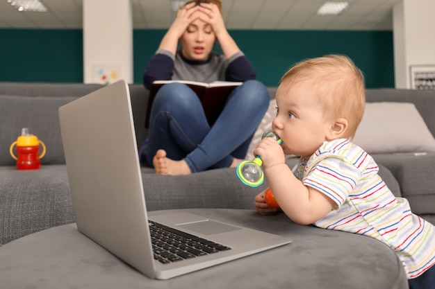 Cute little baby with laptop with tired mother at home