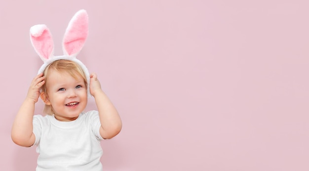 Carino piccolo bambino con orecchie di coniglio su sfondo rosa banner di pasqua