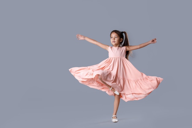 Cute little ballerina girl in pink dress dancing on gray background.