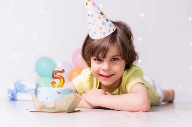 Cute little birthday boy in hat cake with candle five balloons happy birthday