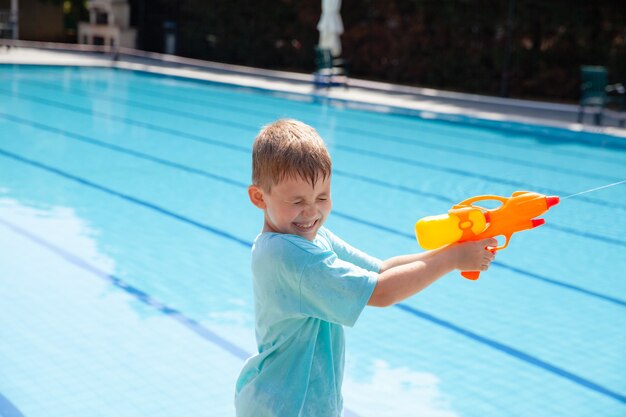 Cute little blond boy having fun on vacation playing water gun fight