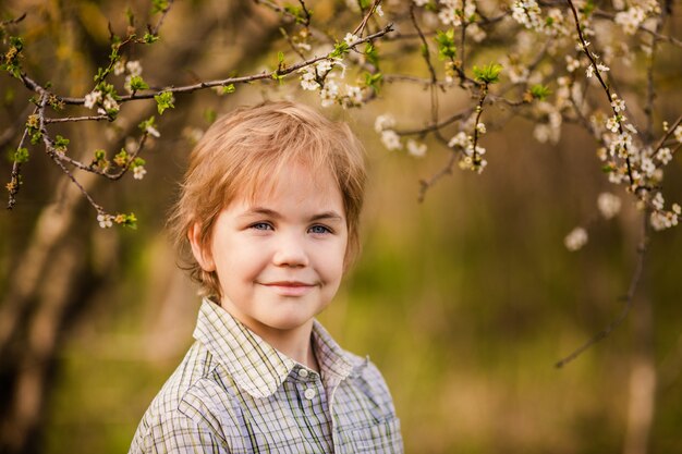 Cute little blonde boy in the spring country with yellow daffodils