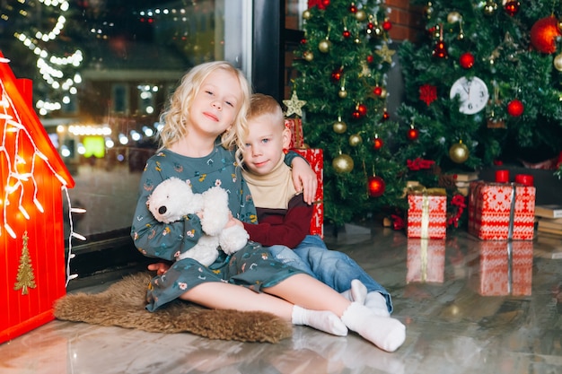 Cute little blonde brother and sister posing at the Christmas tree