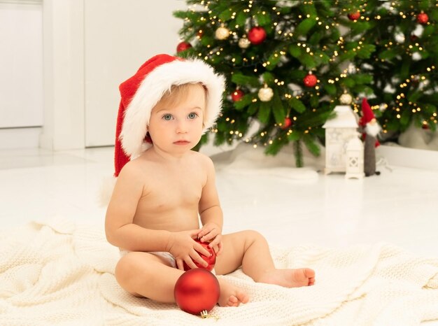 Una graziosa bambina bionda caucasica di 12 anni indossa un cappello da babbo natale seduto di fronte all'albero di natale