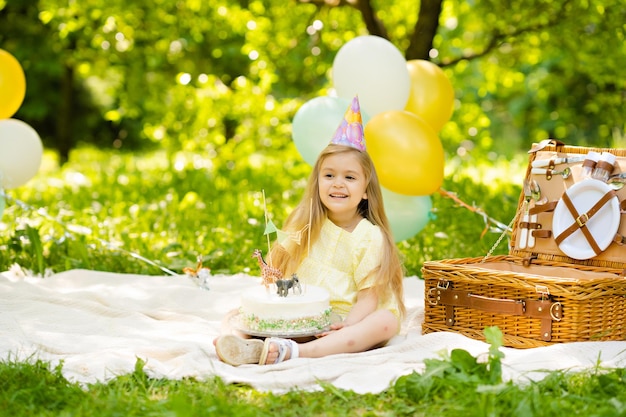 Foto piccola ragazza bionda sveglia che celebra un compleanno nel giardino che tiene una torta di compleanno nelle sue mani